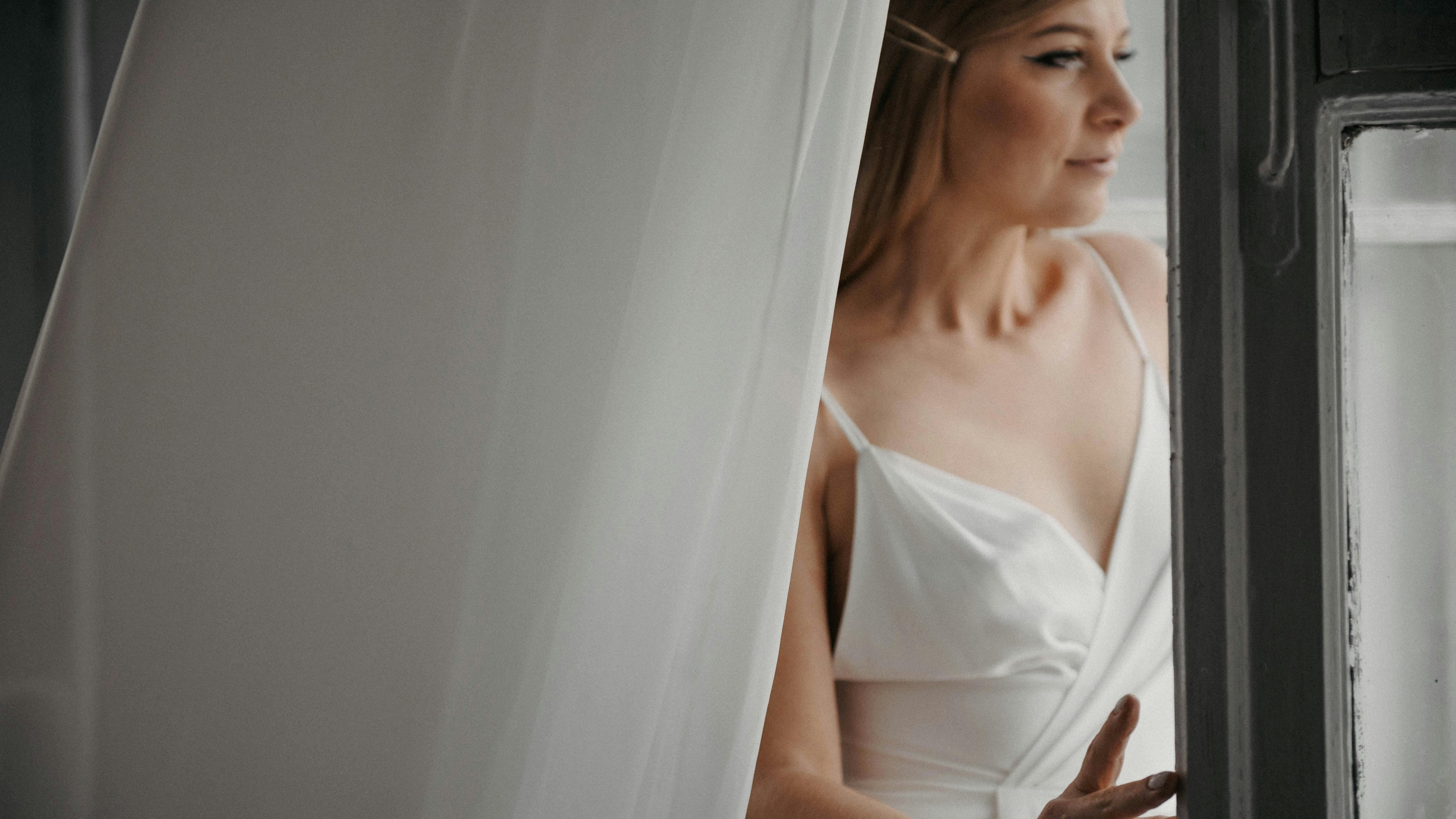 Woman in a white dress peeking out from behind a curtain